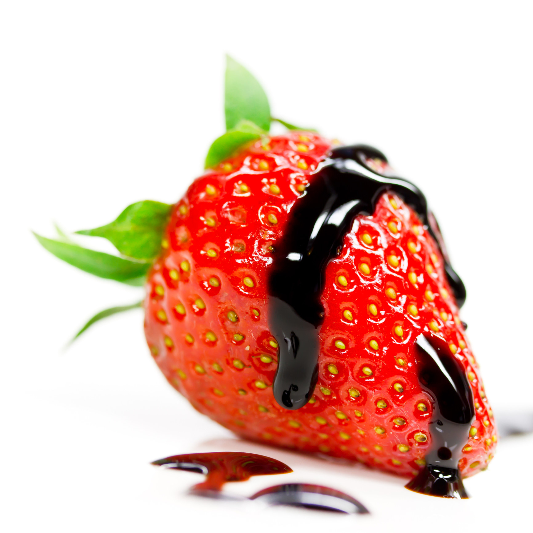A close up shot of a strawberry with a drizzle of balsamic vinegar on top on a white background.