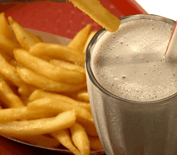 An animated GIF of a hand dunking a french fry inside a milkshake next to a plate of fries.