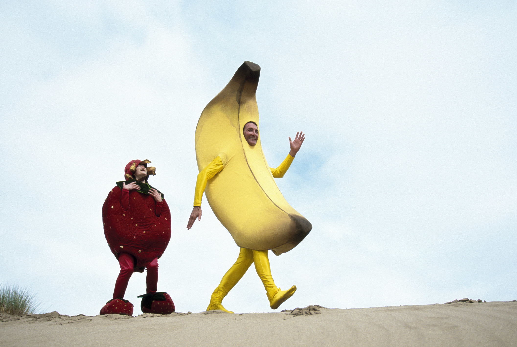 Man dressed as a banana and woman dressed as a strawberry on a beach