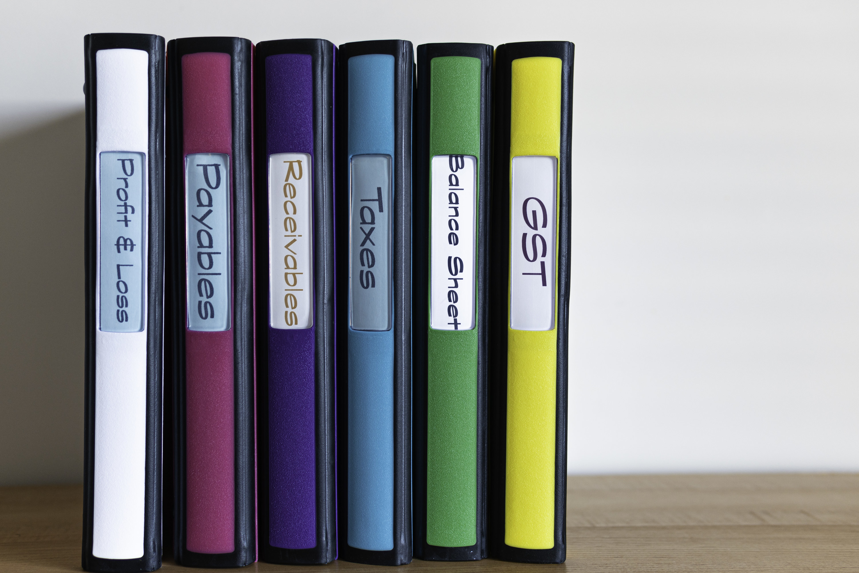 A set of color-coded and labelled binders standing upright on a wooden table