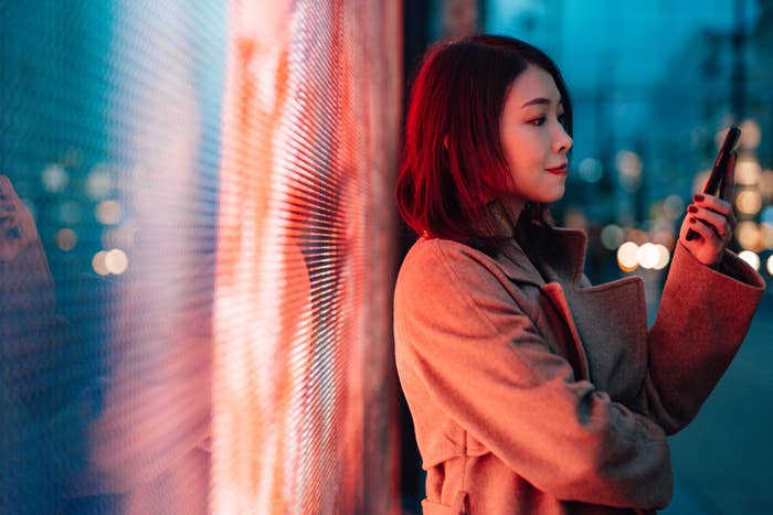Young Woman With Smartphone Standing Against A Digital Display