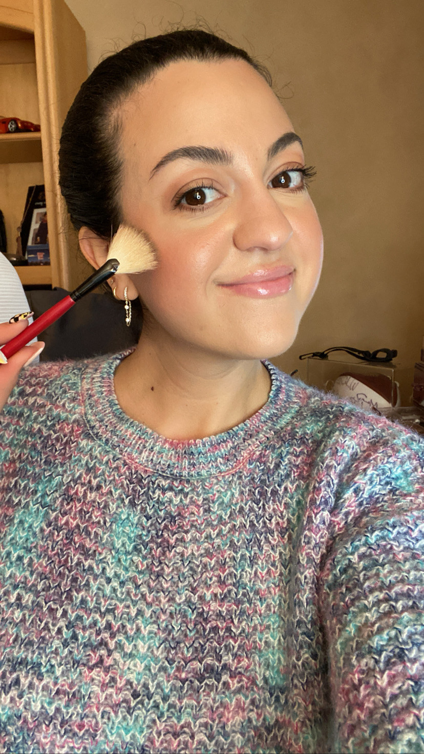 The author applying highlighter onto her cheekbones using a fan brush