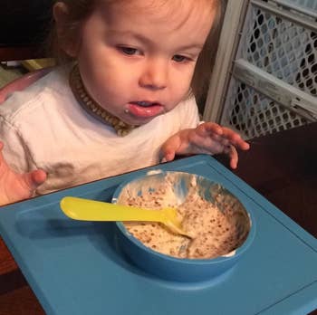 reviewer's photo of their child eating oatmeal from the blue silicone bowl