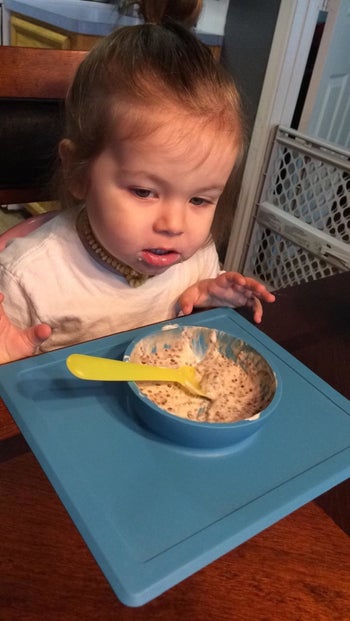 reviewer's photo of their child eating oatmeal from the blue silicone bowl