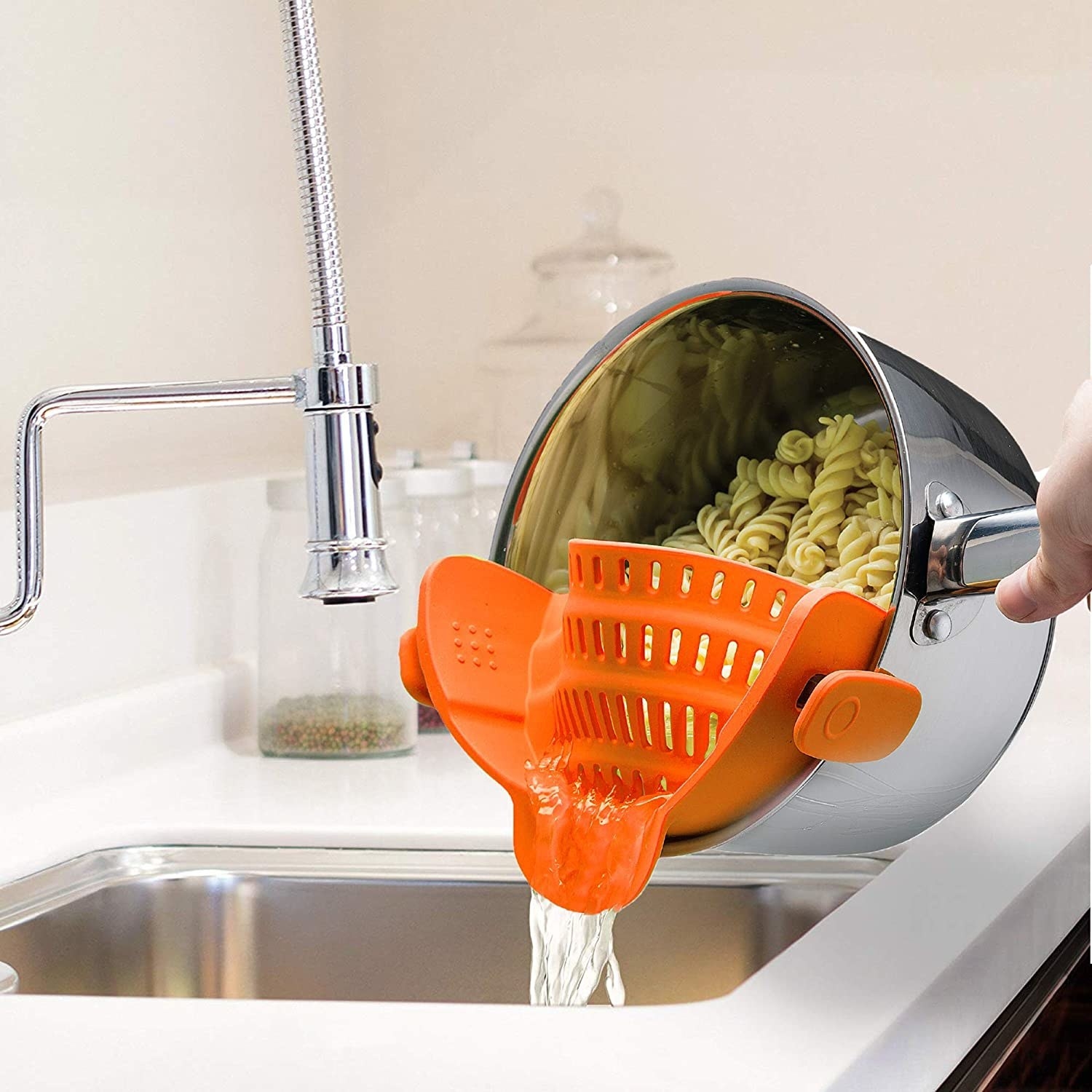 orange snap-on colander straining a pot of pasta into a sink