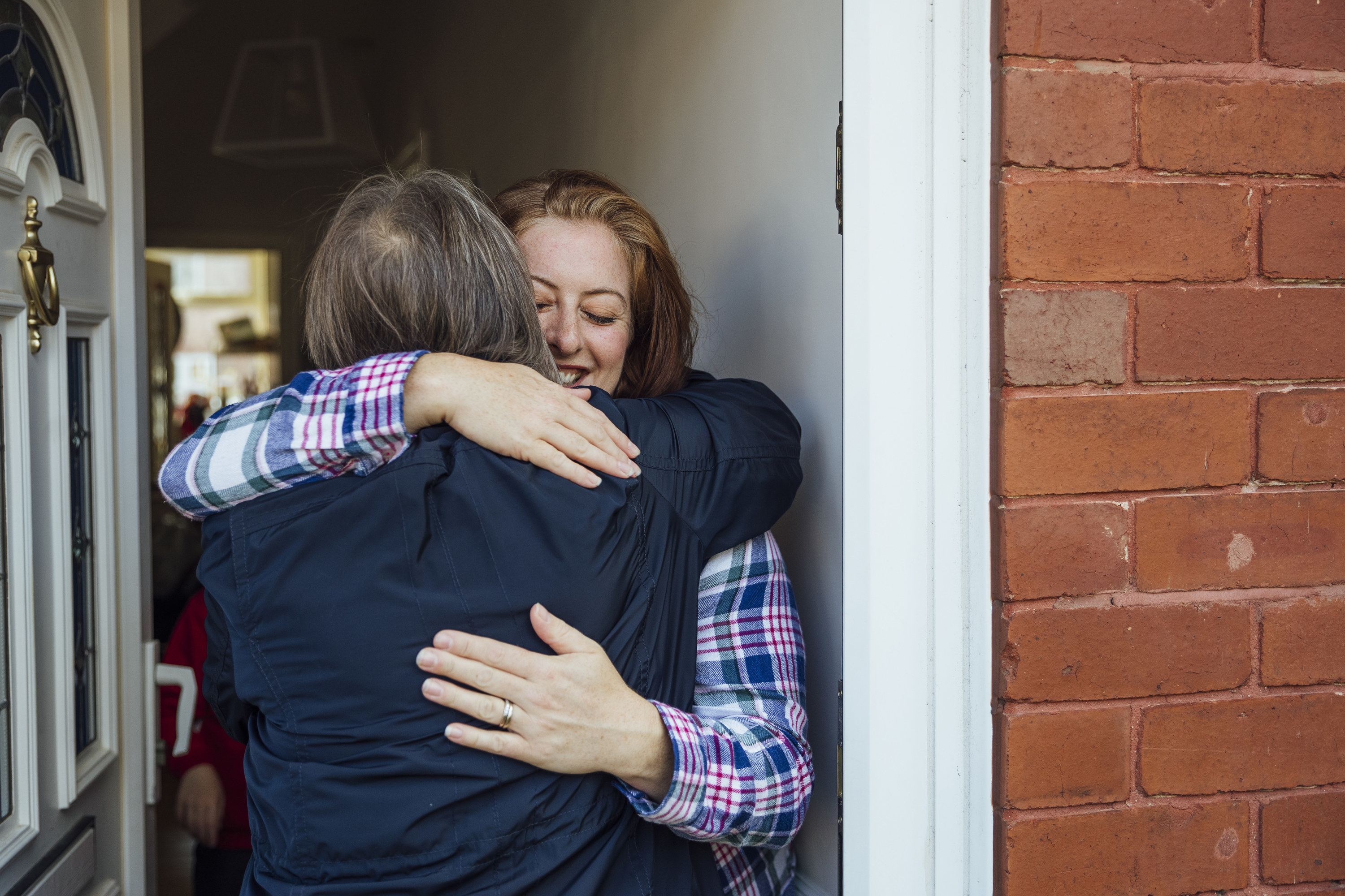 Two people hugging one another at someone&#x27;s front door