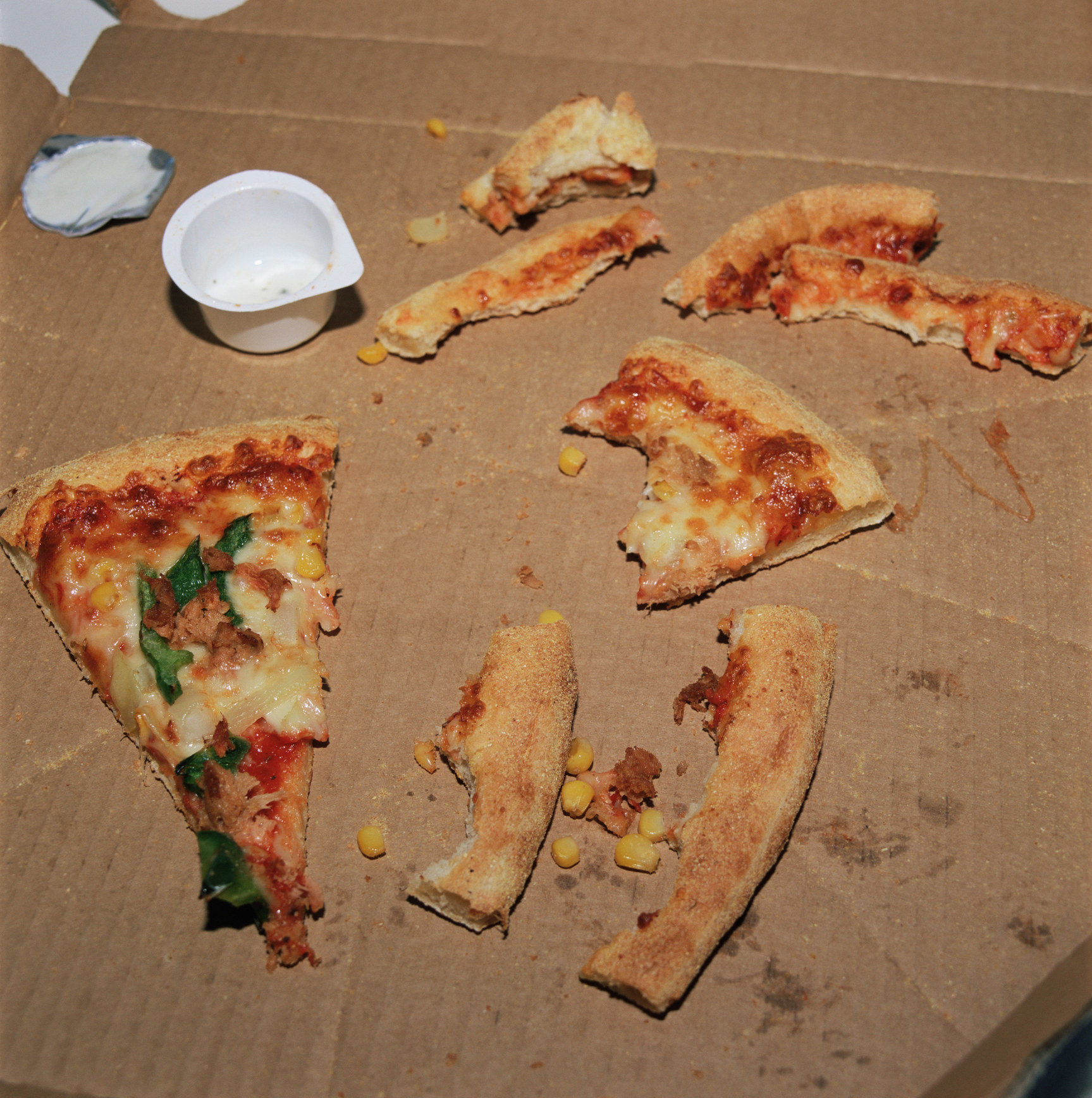 Partially eaten pizza slices with an small open container of ranch dressing