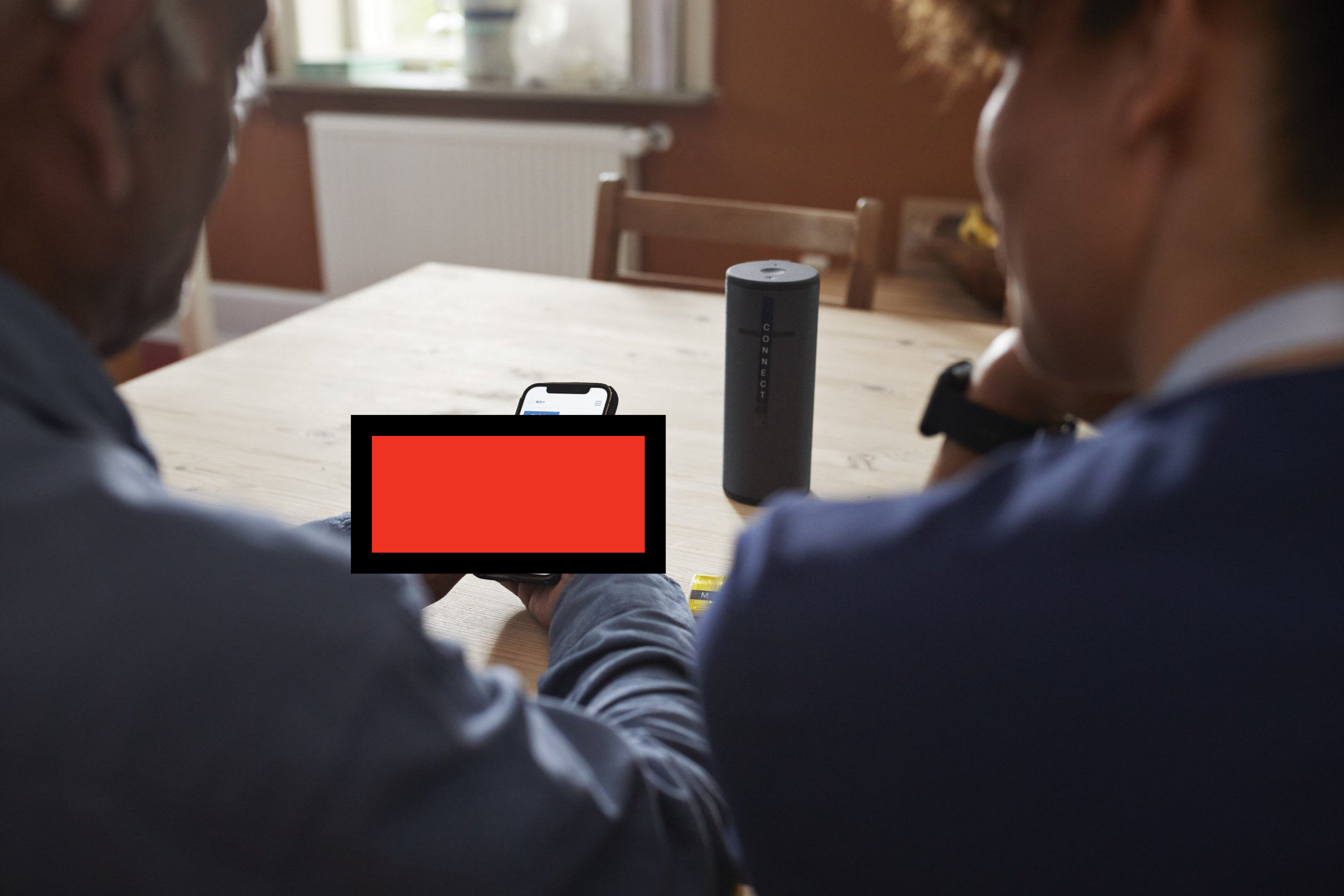 Two people sitting at a table looking at a cellphone that haas been covered