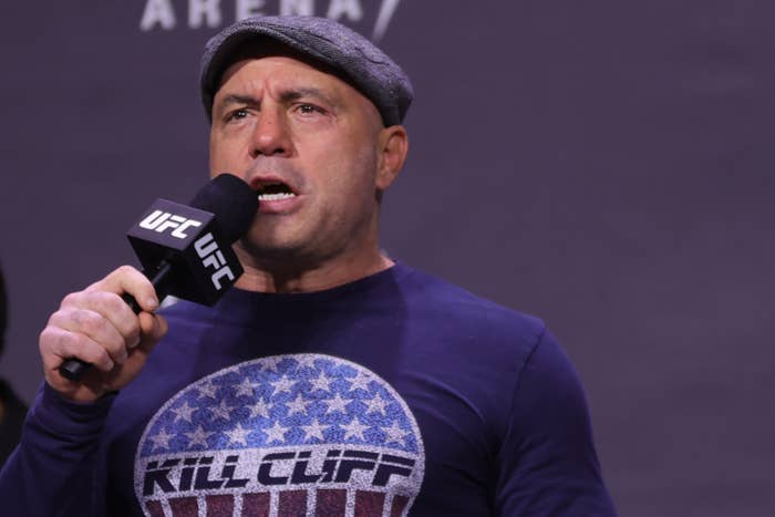 Rogan holds a "UFC" microphone as he speaks into it