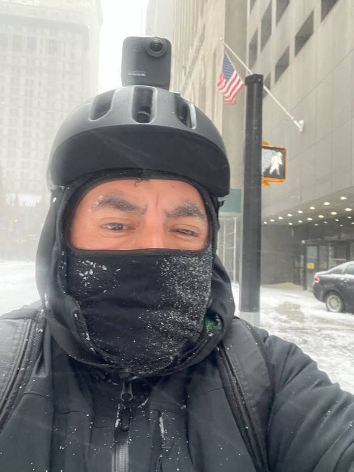 Close-up of man with hooded jacket, helmet, and face covering on a snowy street