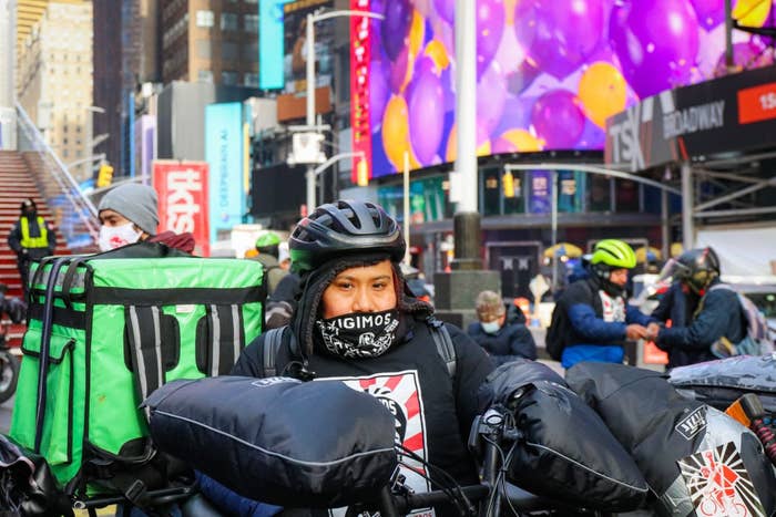 A person with a helmet and face covering in TImes Square with other helmeted riders