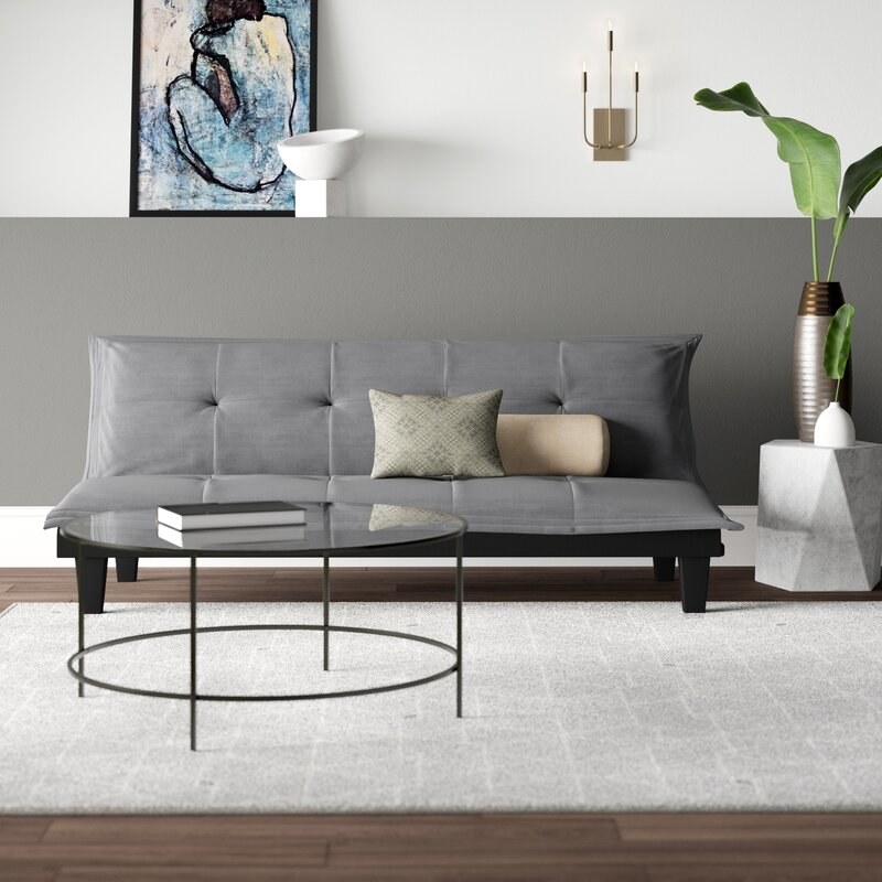 A grey futon with rug and coffee table