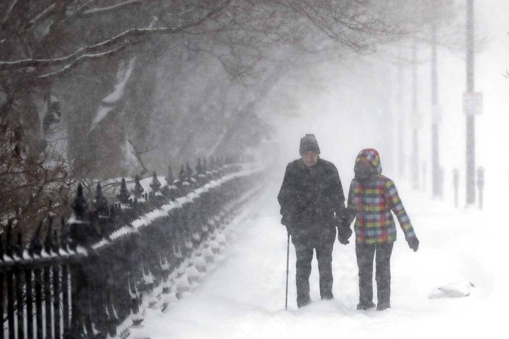 Two people, one holding a cane, hold hands along a snowy street
