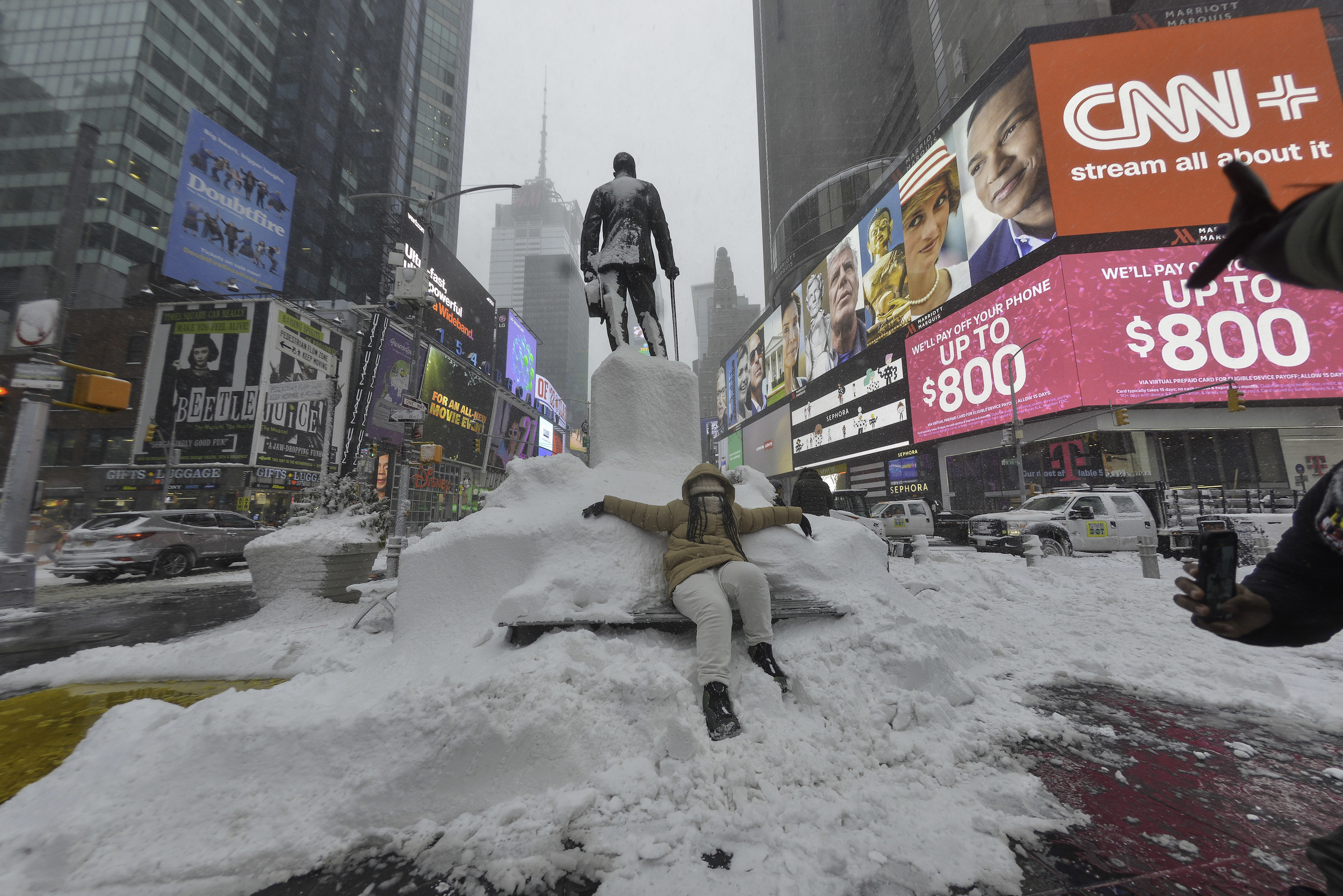 A person sits on a snow-covered bench in Times Square