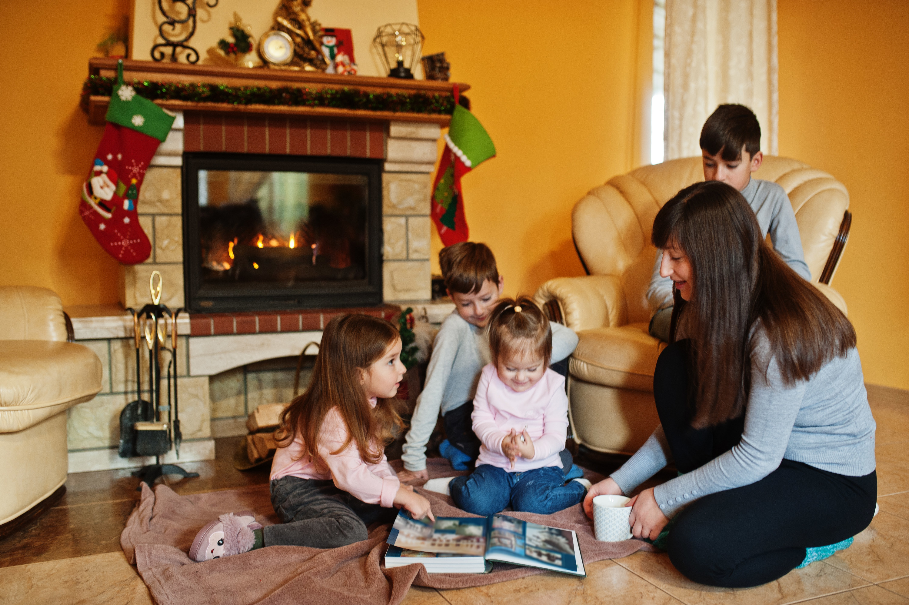 A mom and her four young kids reading a book while sitting on the floor by the fireplace