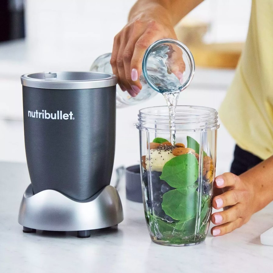 Model pouring water into blender cup filled with ingredients