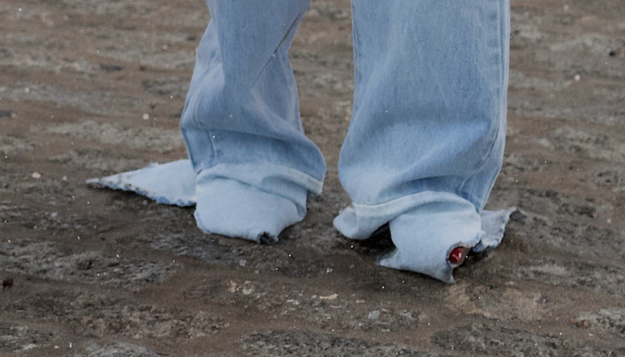 A closeup of Rihanna&#x27;s jeans which are oversized and ripped at the bottom and completely covering her feet