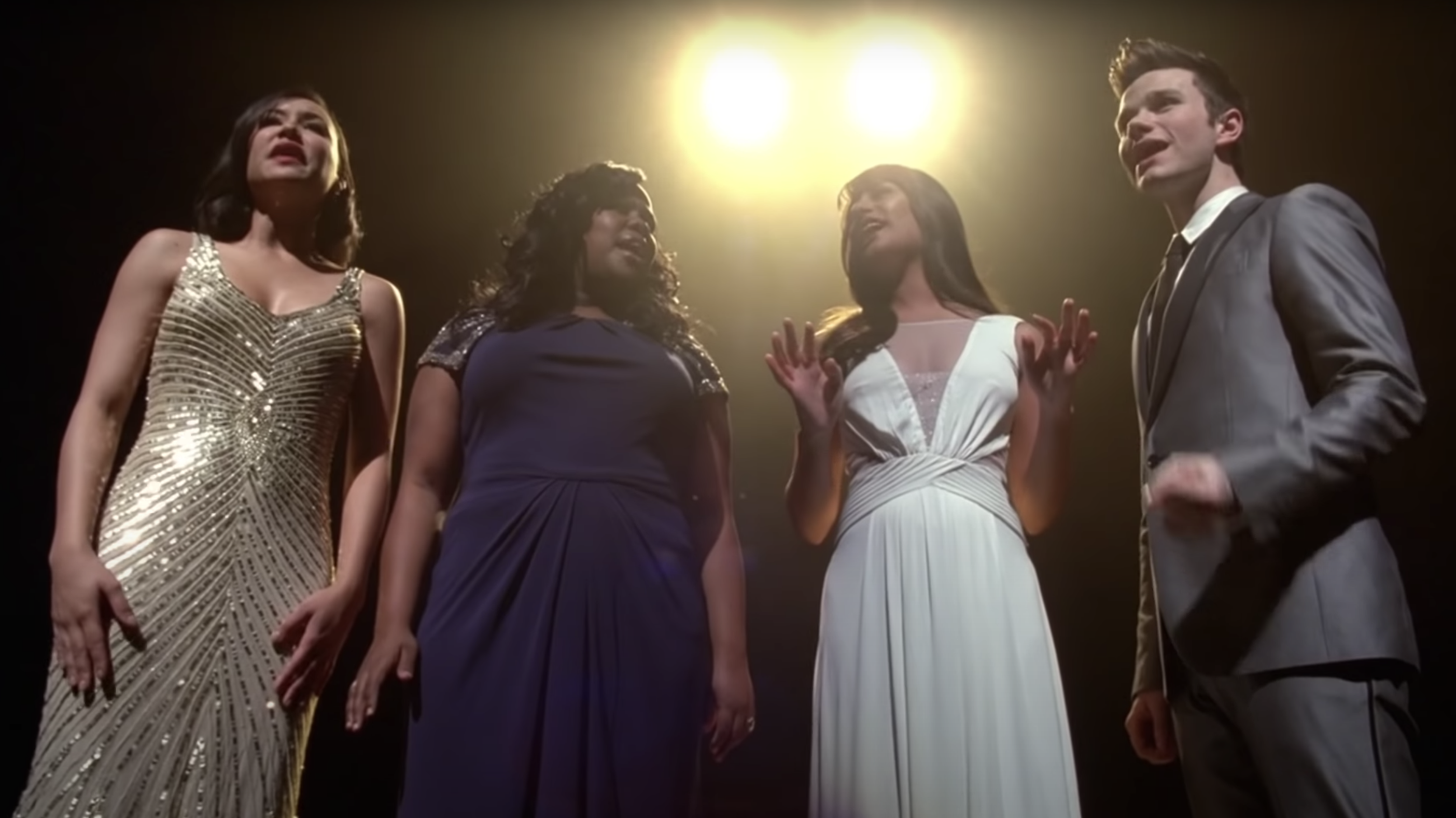 Mercedes, Santana, Rachel in gowns and Kurt in a suit all performing onstage