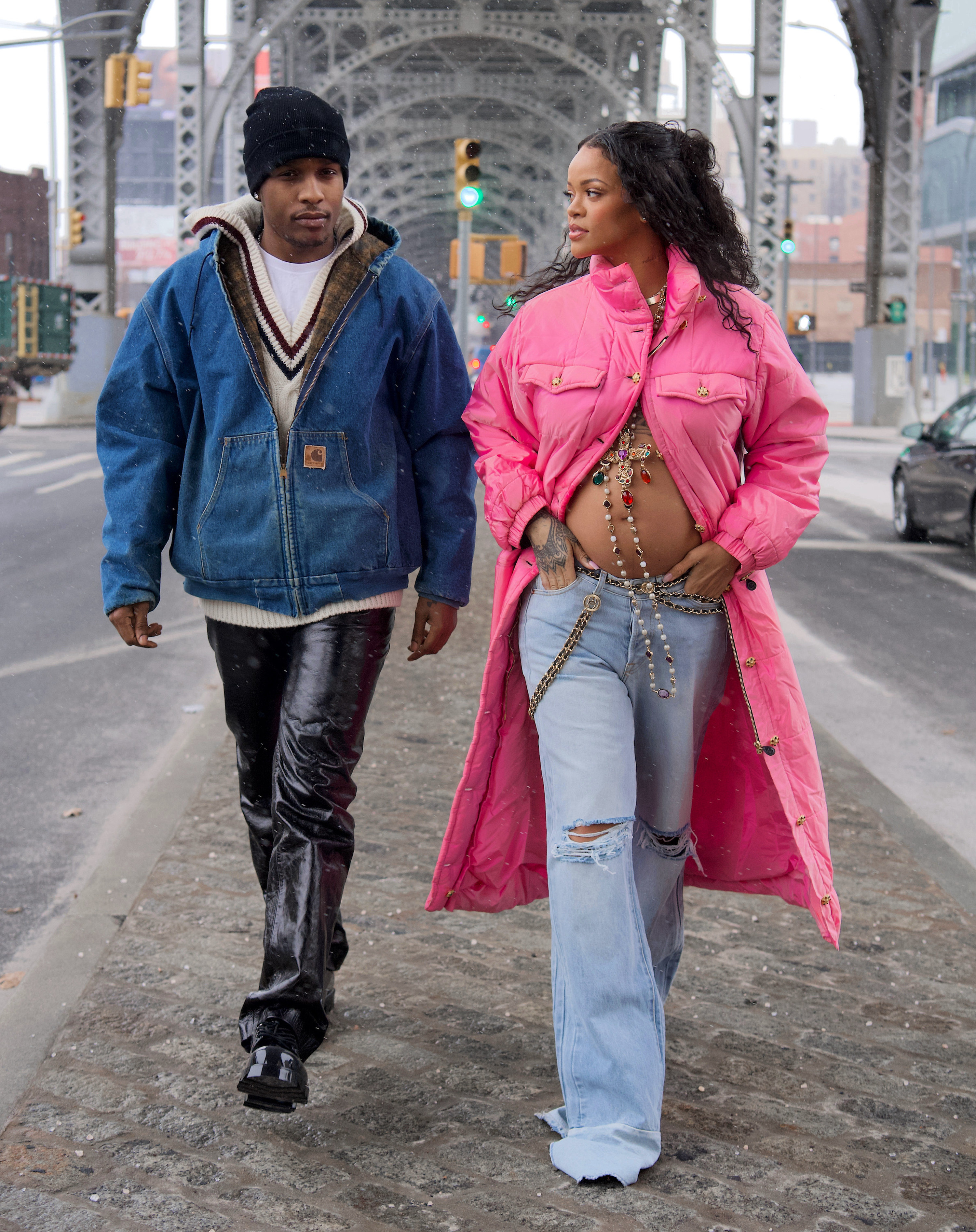 Rihanna is wearing a long bright coat that&#x27;s unbuttoned at the bottom to show her exposed belly bump and ripped jean and a long necklace featuring multicolored gems