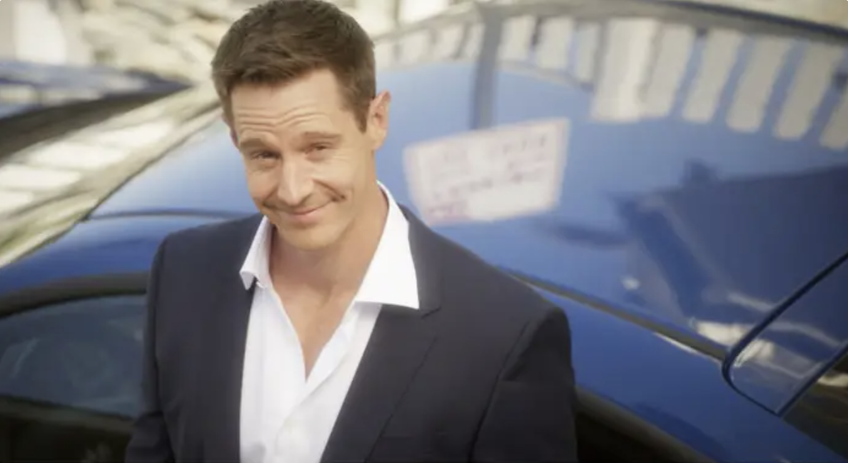 Jason Dohring smirking as he stands next to a car