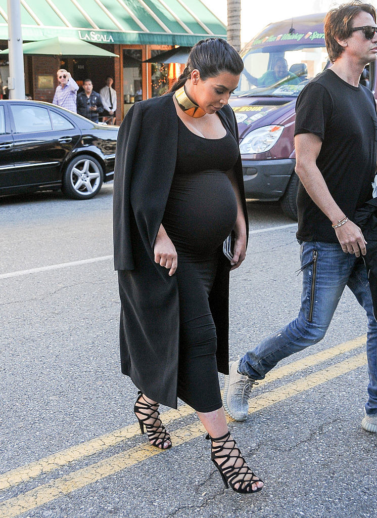 A pregnant Kim walking across a street while wearing an ankle-length dress and matching jacket