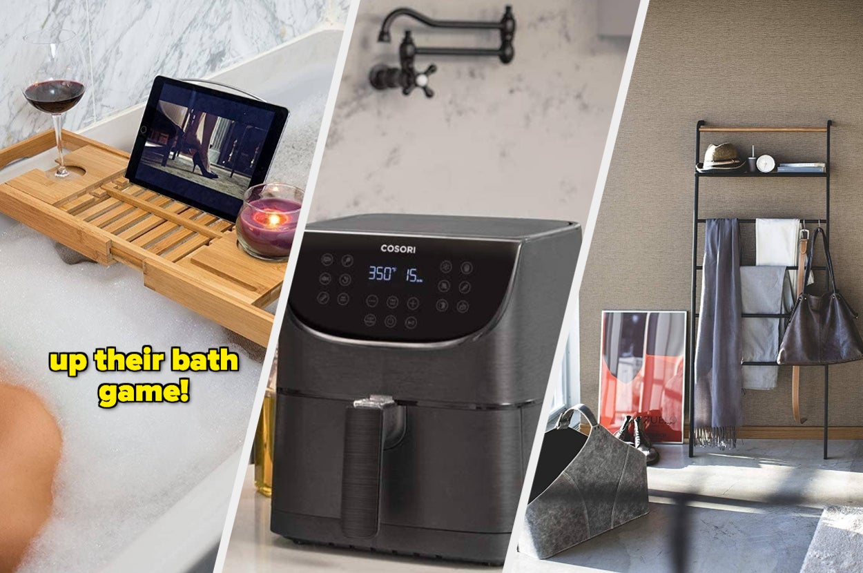 A person in the bath with a bamboo bath tray holding a tablet, a candle, and a wine glass, an air fryer on a counter, and a ladder shelf in a trendy room