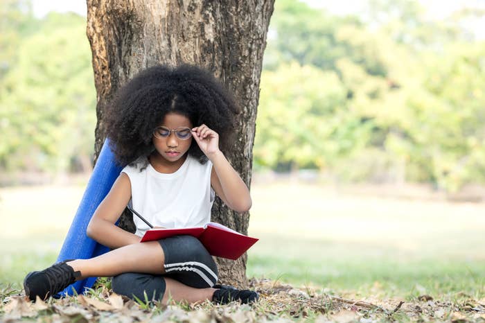 Teenager leaning against a tree in the park while reading a book at park
