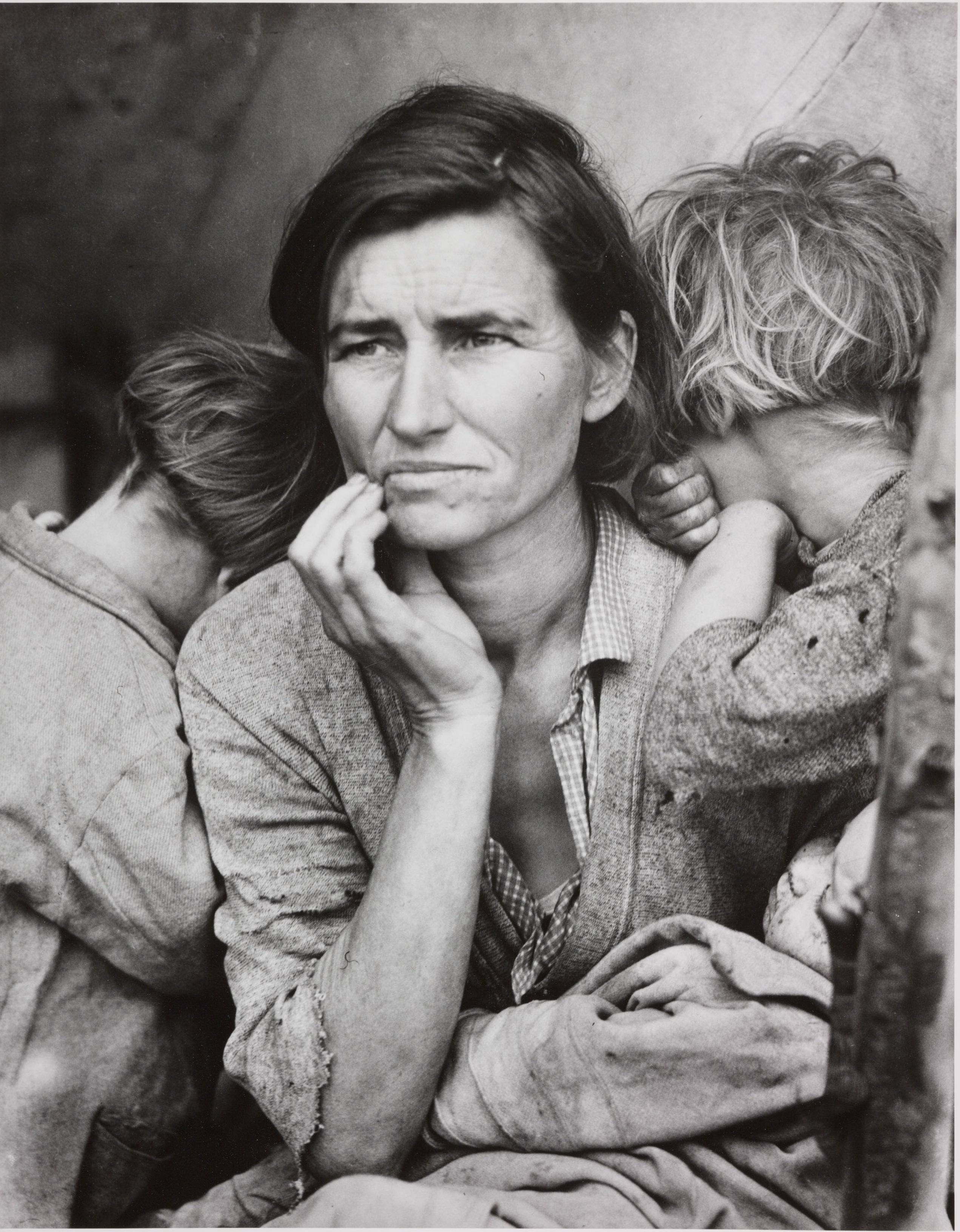 a mother holds her hand to her face in the depression era as two children hide their faces on her 