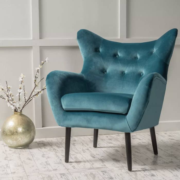 The plush teal chair has seven button pleats and angled arms and a back with four dark wooden legs
