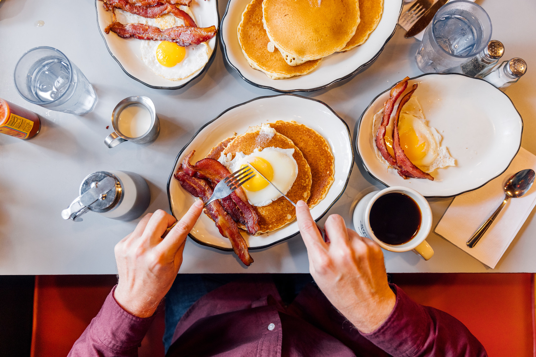 Man eating pancakes with bacon and eggs in a traditional American diner.