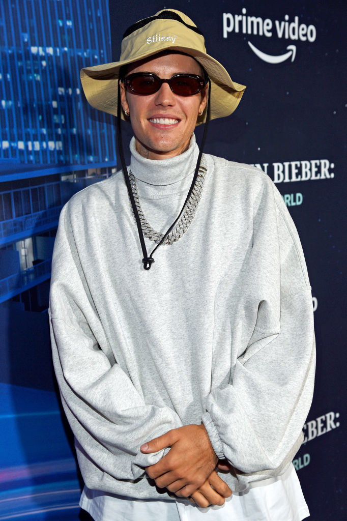 Justin wearing a bucket hat on and a sweatshirt over a shirt and a diamond chain