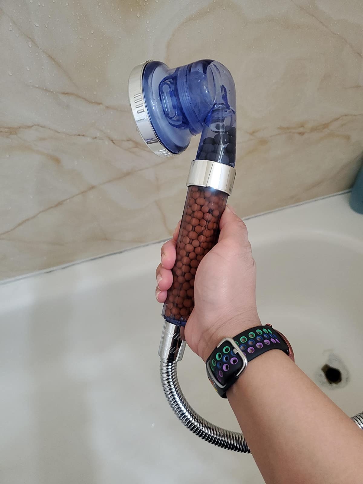 reviewer holding the shower head, which has mineral beads in it that filter and clean the water