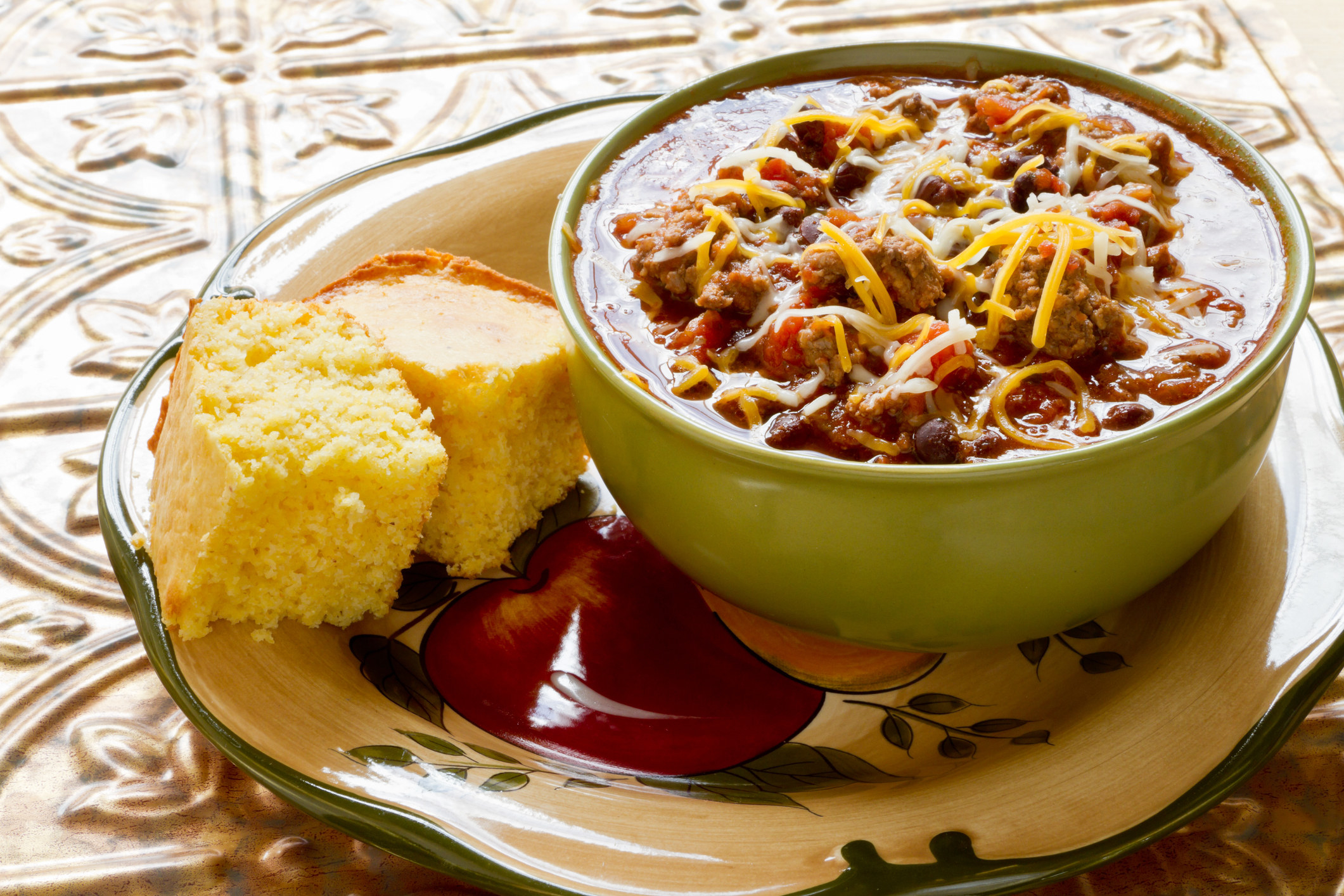 Bowl of black bean chili with shredded cheese and corn bread.