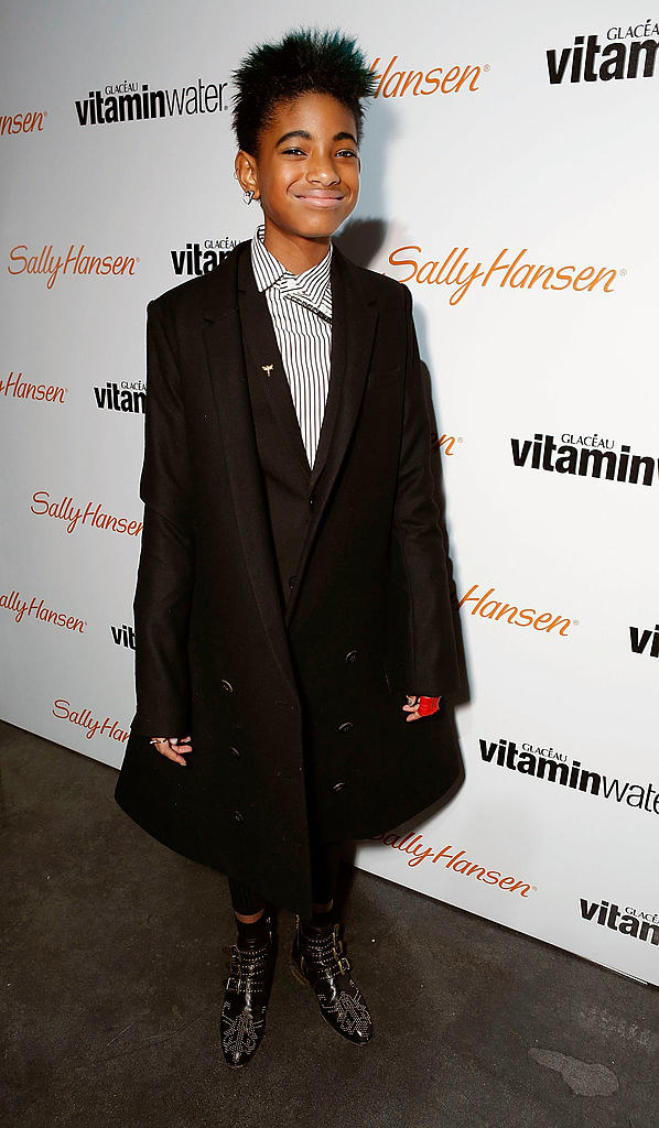 Willow smiling at a vitamin water party in a long coat and bedazzled boots