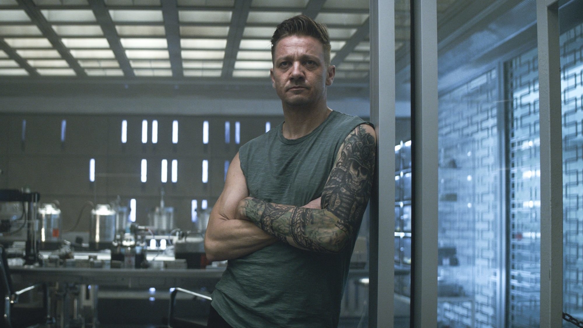 Clint Barton wearing a grayish tang-top with his sleeve tattoo showing. 