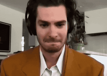 Andrew Garfield with headphones on bopping and moving around with a little smirk on his face during his interview with Jimmy Fallon