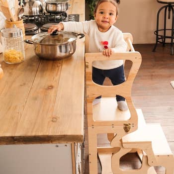 child standing on wooden learning tower in the kitchen