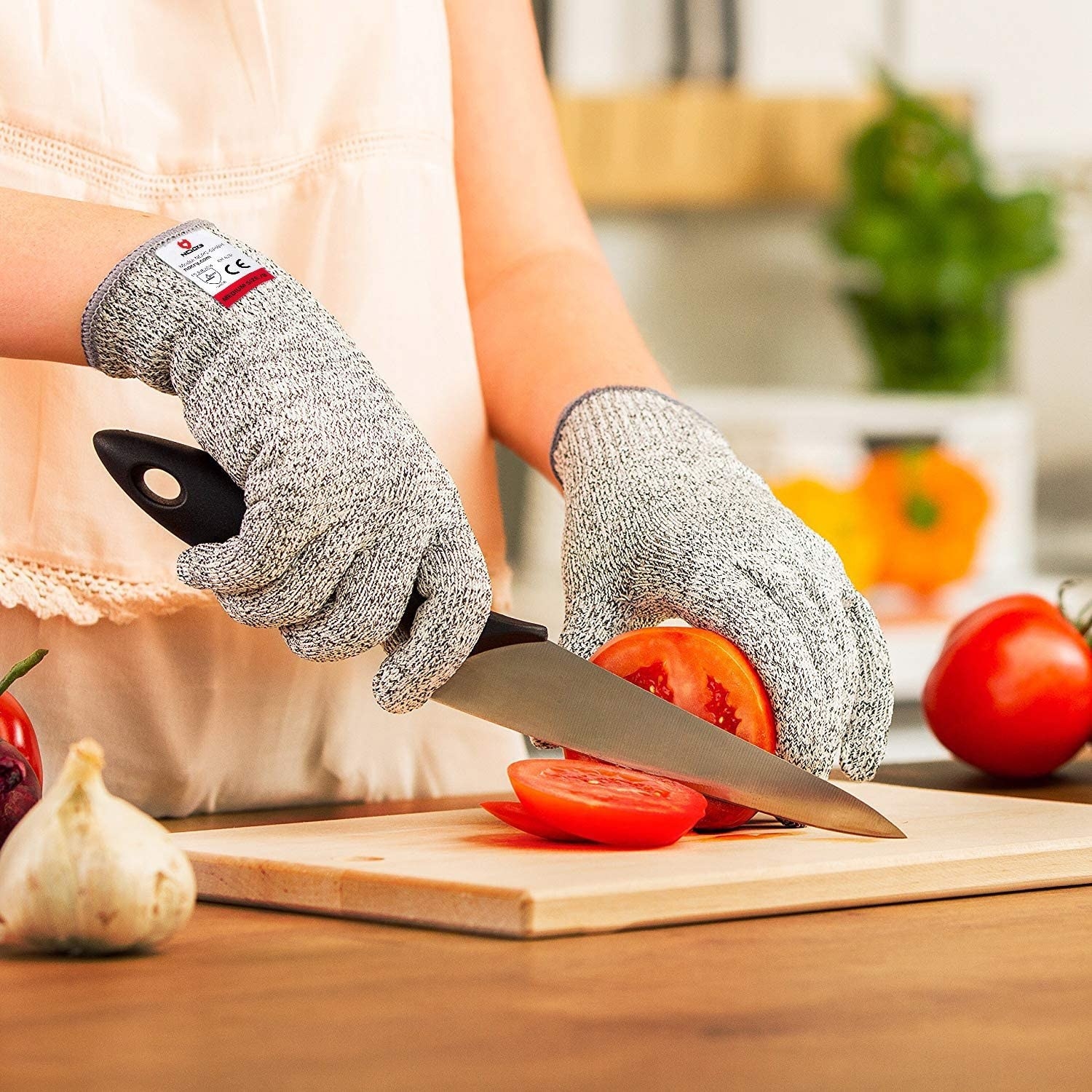 A person wearing  thick gloves while slicing a tomato with a large knife