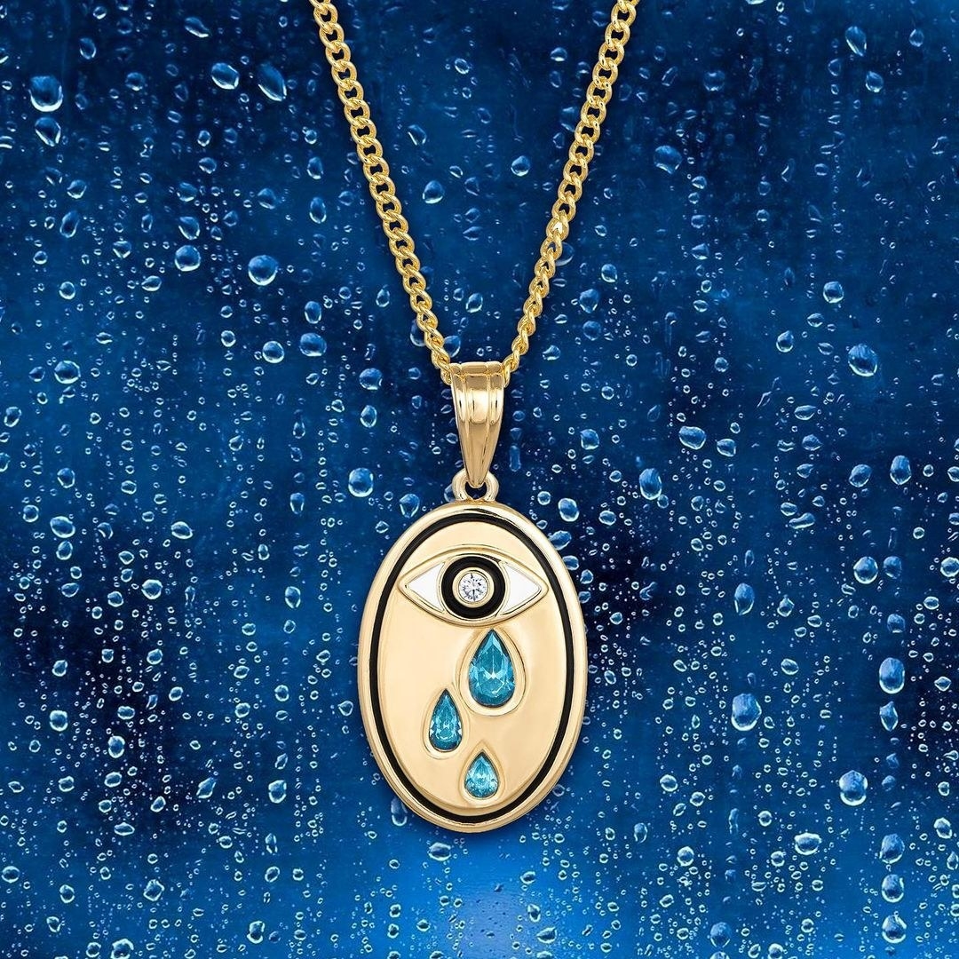 a gold necklace with an oval charm featuring an eye and three tears