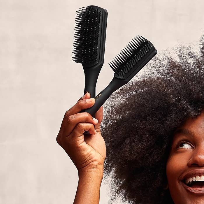 a person holding up two of the shower brushes next to their textured hair