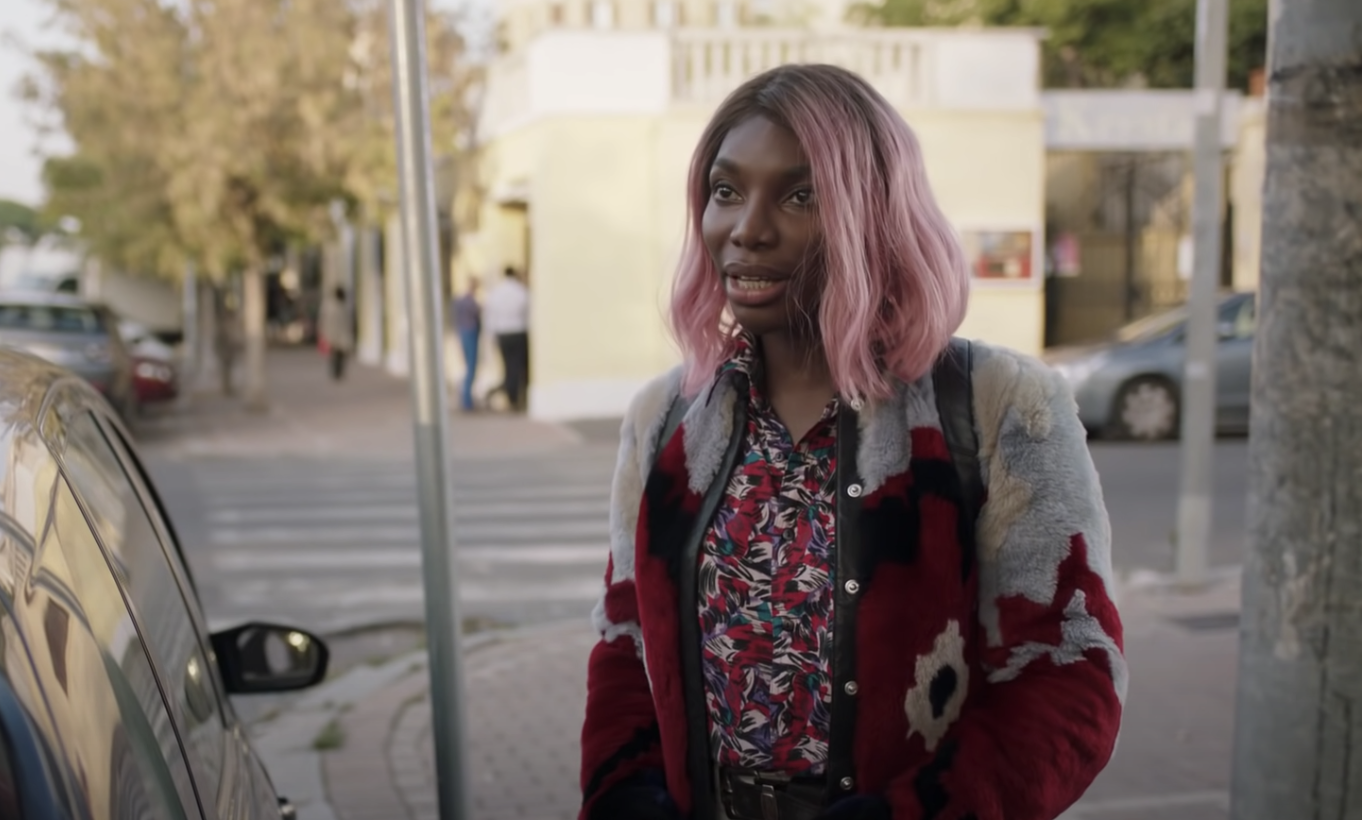 Michaela Coel is outside standing next to a car