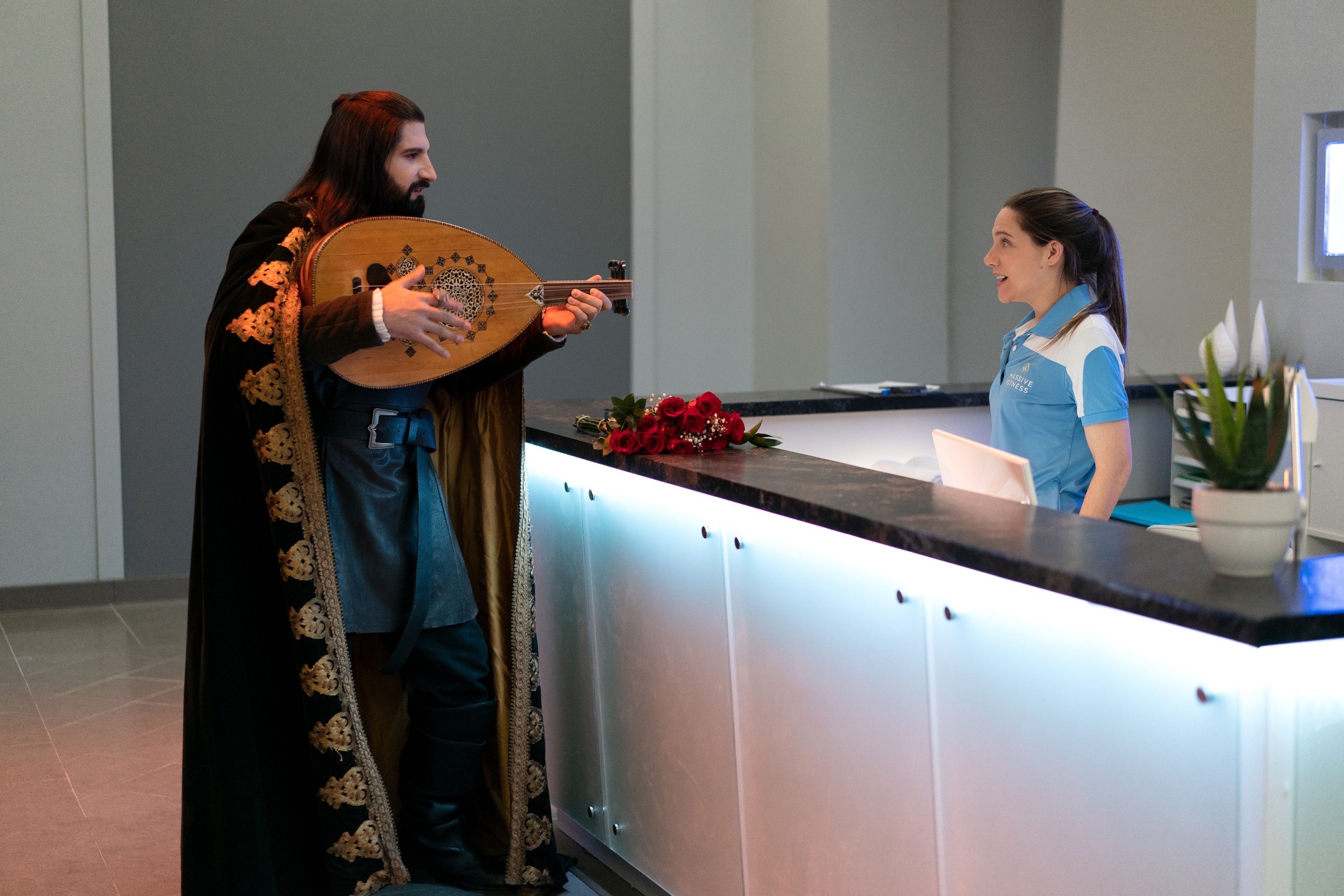 Nandor plays a lute guitar to the front desk receptionist at the gym