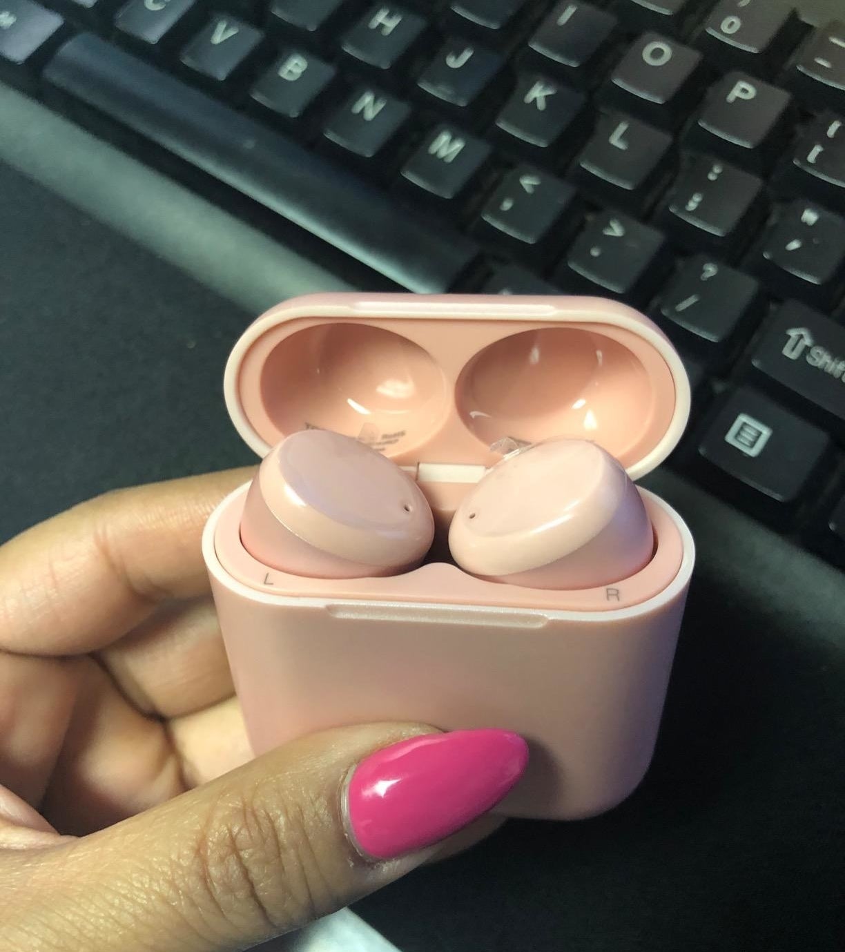 reviewer holding up rose gold earbuds in matching charging case