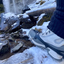 Side view of a reviewer's boot wearing the black grip while walking over snow covered rocks