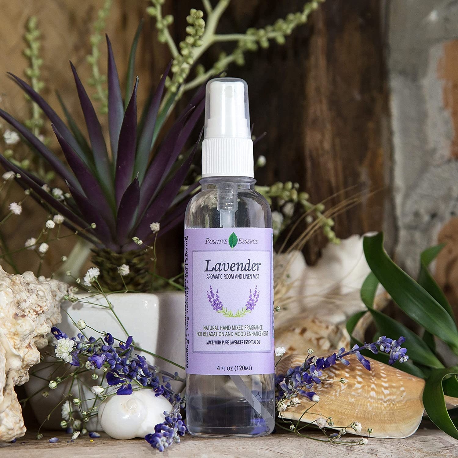A bottle of lavender spray on a table surrounded by shells, plants, and fresh lavender