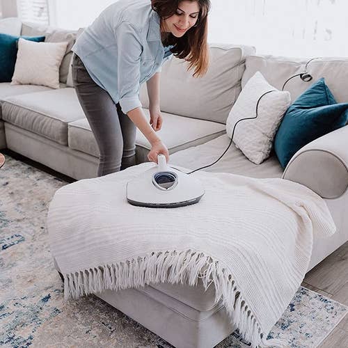 person cleaning a throw blanket with the plugged in vacuum