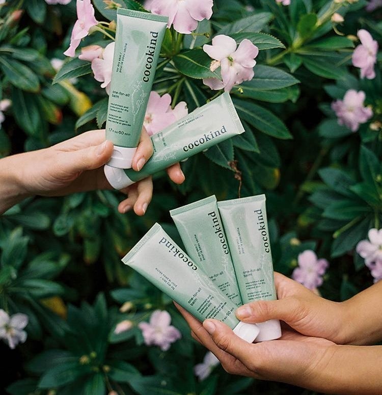 Two pairs of hands holding tubes of the balm