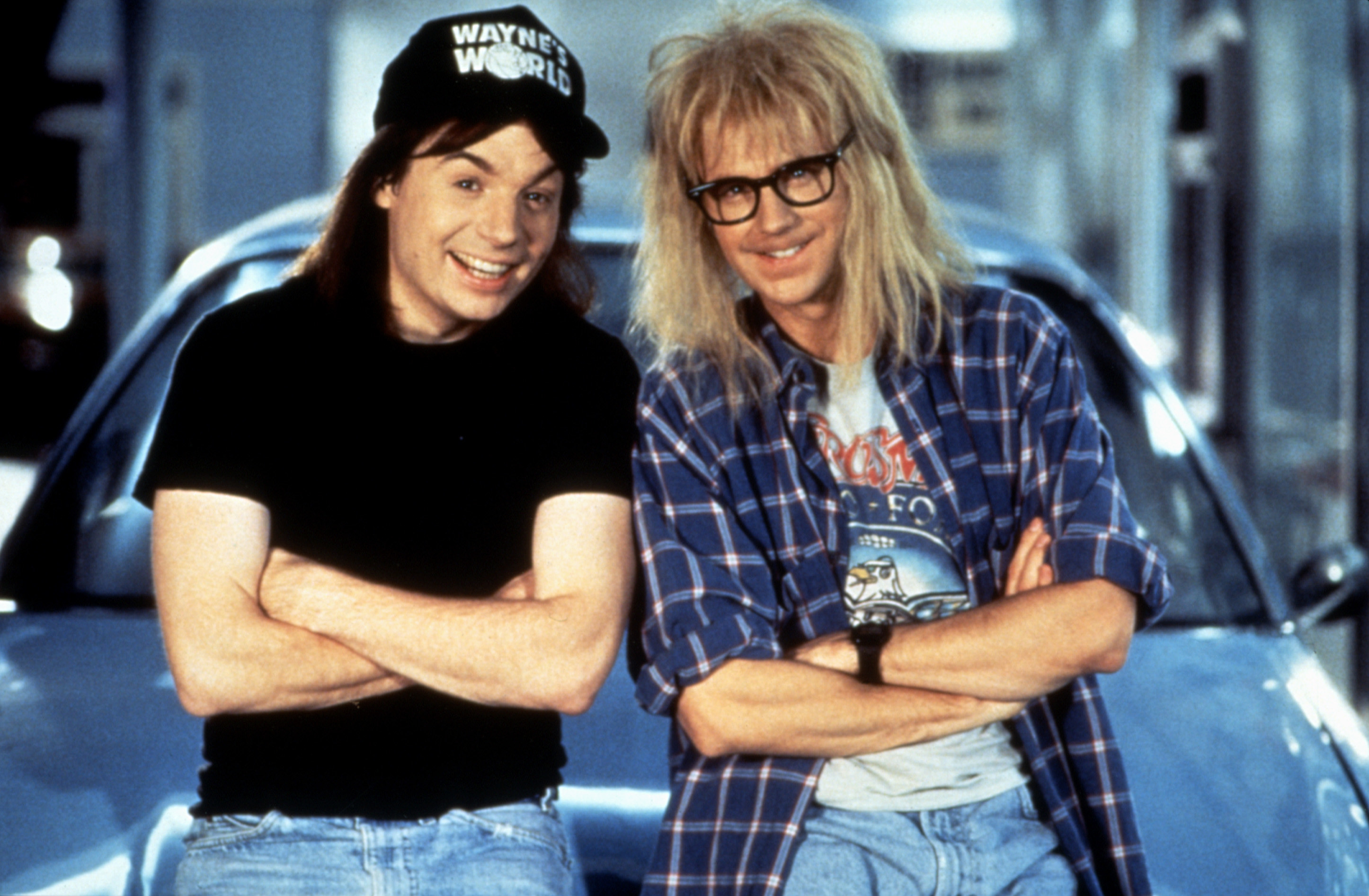Wayne and Garth leaning against a car and smiling