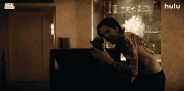 Tommy setting up a camera in the bedroom before running over to Pam who's on the bed in a scene from the series