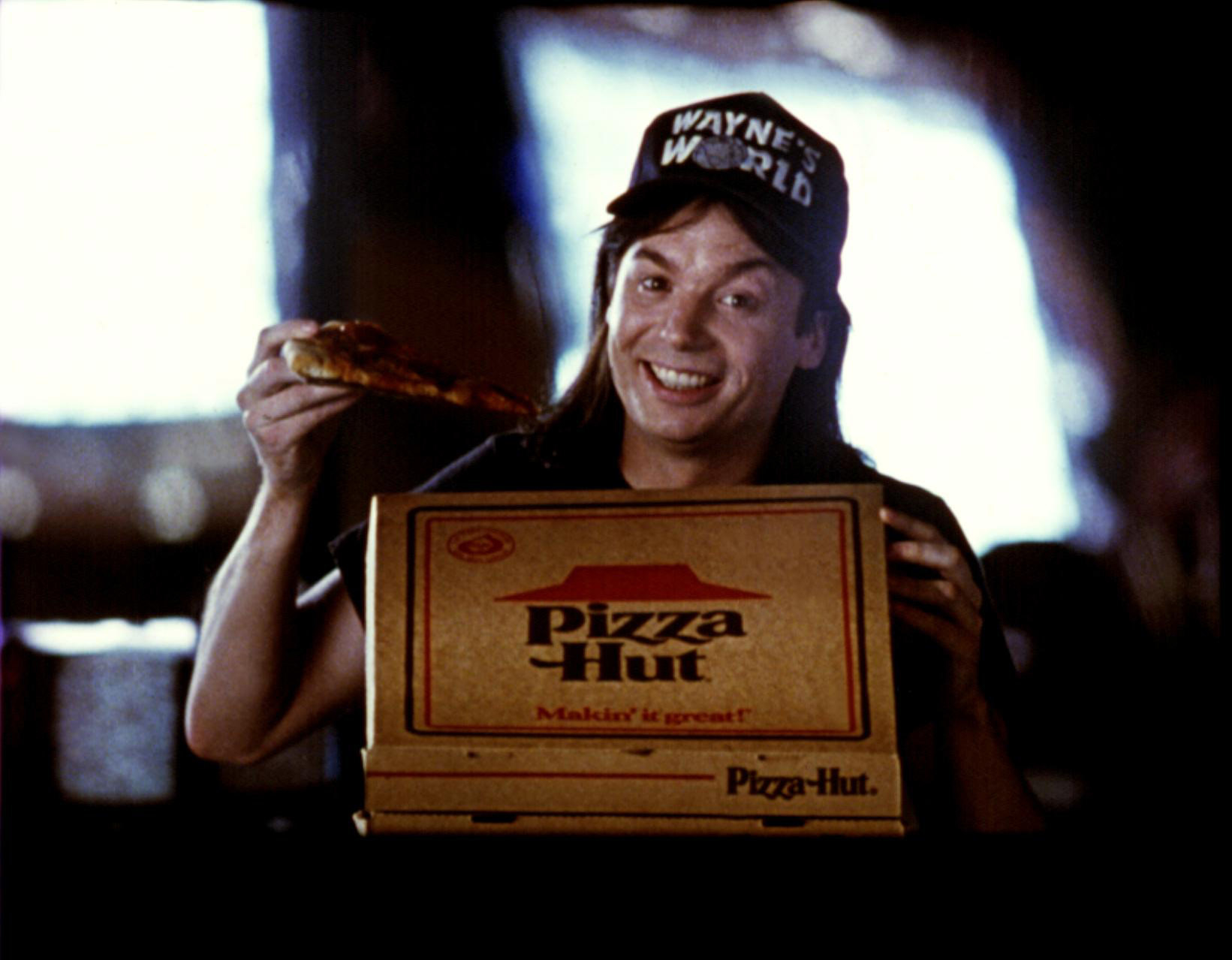 Wayne eating a slice of pizza from a Pizza Hut box and smiling